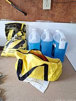 Lot overview with three washer fluid jugs, Windsor ice melt bag, yellow bag with booster cables