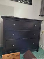 Front view of black laminate three-drawer dresser