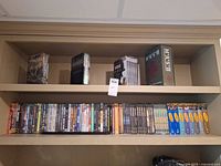 Two-shelf view showing five box sets on top shelf and full row of single DVDs on lower shelf