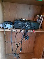 Shelf with Xbox console, two controllers, cables, stack of game cases