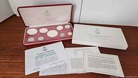 Overview of open presentation case with nine coins, outer slipcase and paperwork