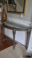 Full view of glass-top demilune console table against wall