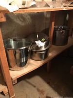 Three stainless steel vessels on shelf: two tall stock pots and one roaster