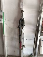 Full view of come-along winch hanging on wall showing overall construction, cable and hooks