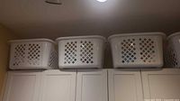 Three white plastic laundry baskets on top of cabinets