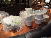 Stack of plates with plastic packaging beside stacked teacups and saucers