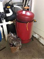 Full view of red barrel smoker beside plumbing