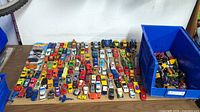 Full view of table with rows of die-cast vehicles and blue bin