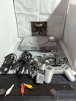 Front view of PS1 console with controller, cables, memory card, game