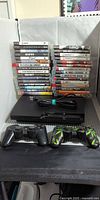 Overall lot showing PS3 console, power cord, two controllers and stacked 31 game cases