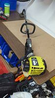Full view of Ryobi gas trimmer on table showing power head, shaft, shoulder strap and fuel tank