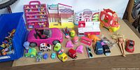 Overall view showing toys spread on table including vehicles, playsets, accessories, doll and bin