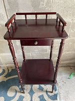 Front view of dark wood two-tier side table with drawer and spindle gallery