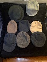 Eight hats displayed on black surface showing variety of colours and textures
