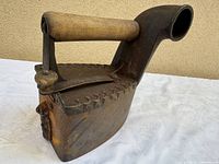 Left side view of cast iron coal iron showing wooden handle, serrated lid and chimney