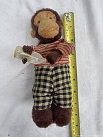 Front view of plush wind-up monkey with bottle, cup and tape measure showing height