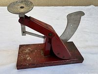 Side view of red metal egg scale showing weighing cup, indicator arm and base