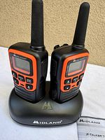 Two Midland X-Talker radios in charging cradle with manual visible