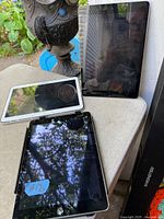 Three tablets on table: two black-bezel iPads and one white-bezel Samsung
