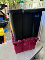 Two stacked plastic totes, black on maroon, lids visible