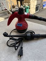 Front view of red and black handheld steam cleaner with hose and power cord displayed