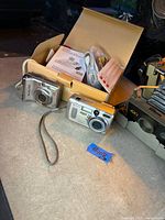 Two compact digital cameras (Canon PowerShot A560, Kodak EasyShare) with strap, partial view of Polaroid 420