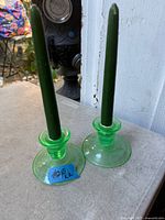Pair of green uranium glass candlestick holders each with a green taper candle inserted