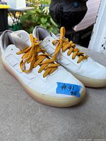 Full view of pair of Adidas shoes with mustard laces and blue tape label