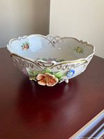 Oblique view showing exterior floral reliefs, gilt rim, bowl shape