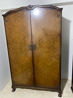 Closed view of Heirloom walnut veneer armoire showing exterior, crown molding, brass hardware, bracket feet on casters