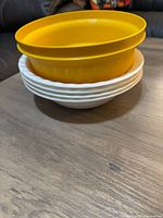 Stack with two yellow plastic bowls atop white scalloped bowls