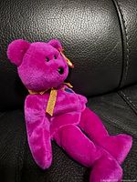 Full view of magenta Millennium bear reclining on black surface