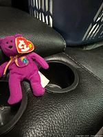 Front view of purple Ty bear on leather seat showing swing tag and body