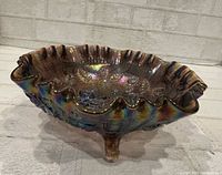 Oblique view showing iridescent finish, ruffled rim, and three feet