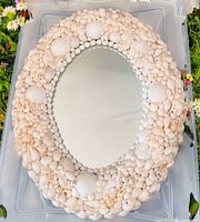 Front view of oval mirror showing full shell-covered frame and reflective glass