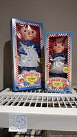 Both boxed Raggedy Ann dolls on shelf