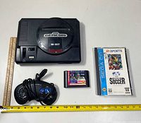 Top view of Sega Genesis console, controller, Tecmo Super Bowl cartridge, FIFA International Soccer Sega CD case, rulers for scale