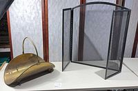 Overall view of brass log holder and black fireplace screen on table