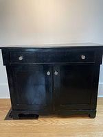 Front view of black painted wood cabinet showing drawer and two doors