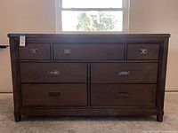 Front view of medium brown seven-drawer dresser with brushed nickel recessed pulls