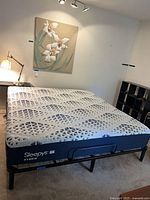 Sleepy’s Hybrid king mattress on black metal platform frame with wall art and desk lamp visible