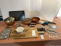 Full lot overview showing bowls, pans, knives, flatware and boards