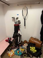 Overall lot showing golf bag with clubs, HEAD racquet, duffel, mesh bag of tennis balls and loose practice balls