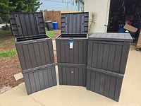 Four of the six dark gray resin storage boxes, two with lids open showing interior