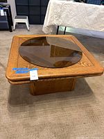 Square oak pedestal coffee table with round smoked glass top resting on surface