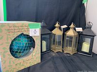 Group shot showing two black lanterns with candles, two bronze lanterns with tags, and boxed gazing ball