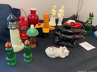 group shot of assorted Avon glass decanters including lighthouse, lanterns, candles, boot, vase, desk, dogs, car, bell, train, ceramic pig