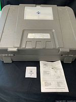 Closed gray case, manual and auction card