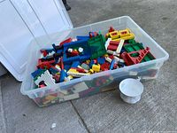 Wide shot of clear tote filled with assorted Lego Duplo bricks beside a teacup for scale