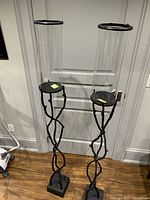 Pair of tall vine-style black metal stands with clear glass hurricane shades
